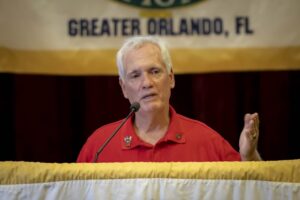 A man in red shirt speaking at podium.