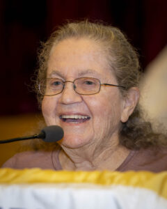 A woman with glasses is speaking at a microphone.