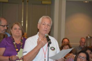 A man is speaking at an event with people behind him.